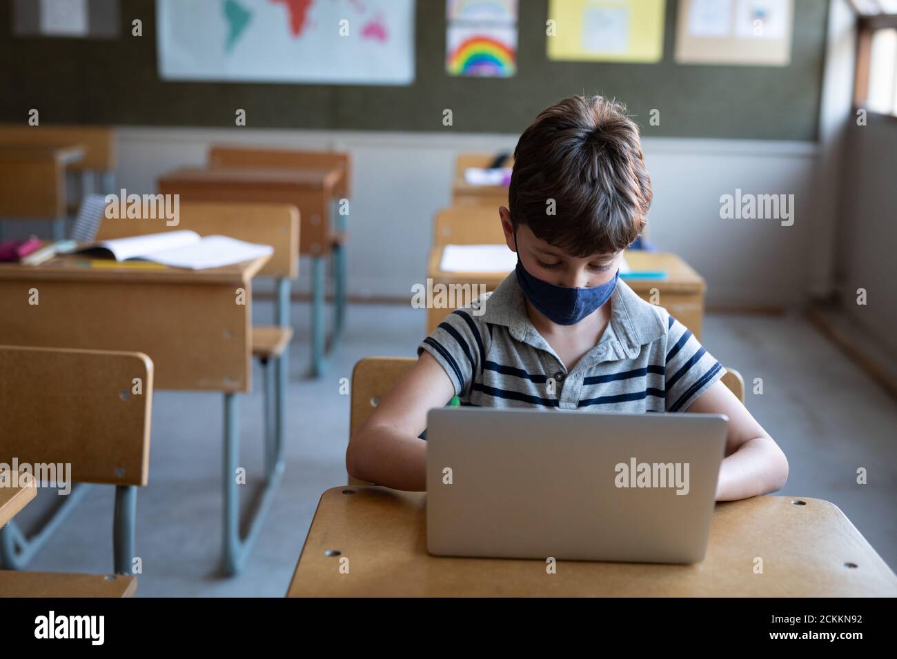 Garçon portant un masque facial avec un ordinateur portable sur son bureau à école Banque D'Images