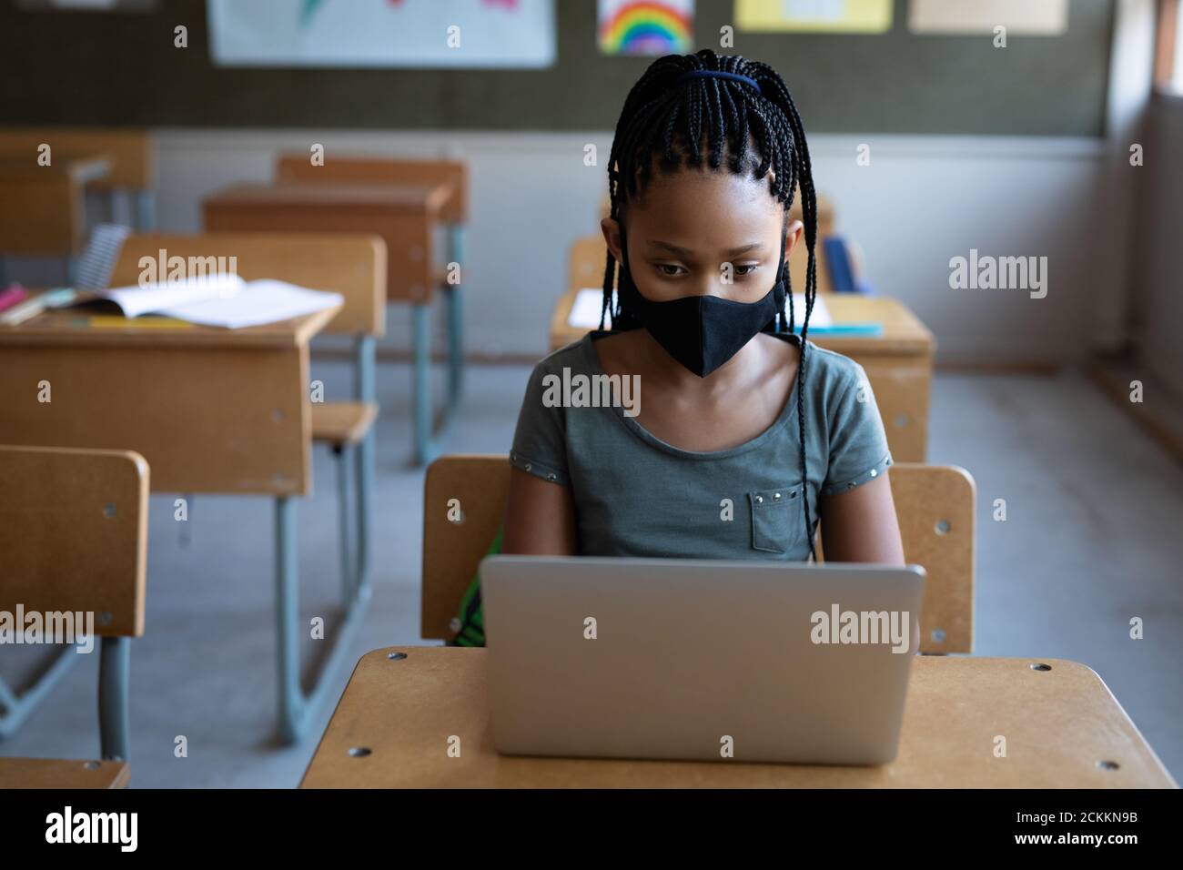 Fille portant un masque facial utilisant un ordinateur portable sur son bureau à école Banque D'Images