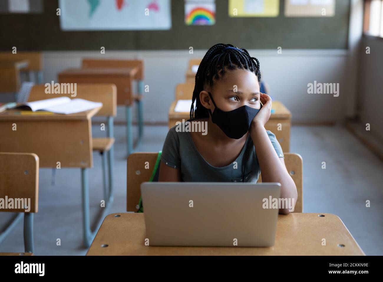 Fille portant un masque facial assis avec un ordinateur portable sur son bureau à l'école Banque D'Images