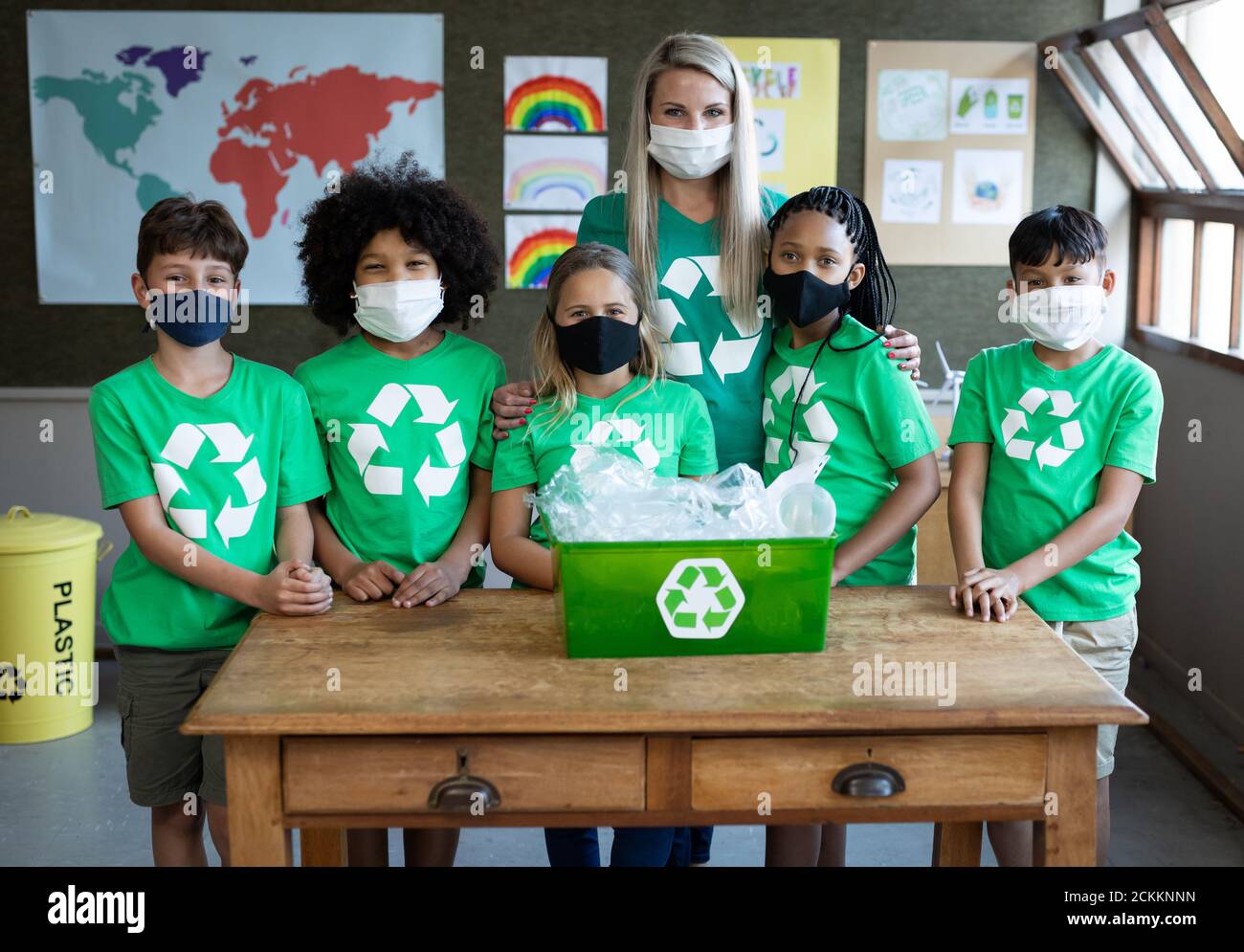 Portrait d'une enseignante et d'un groupe d'enfants portant le visage masques avec récipient de recyclage à l'école Banque D'Images