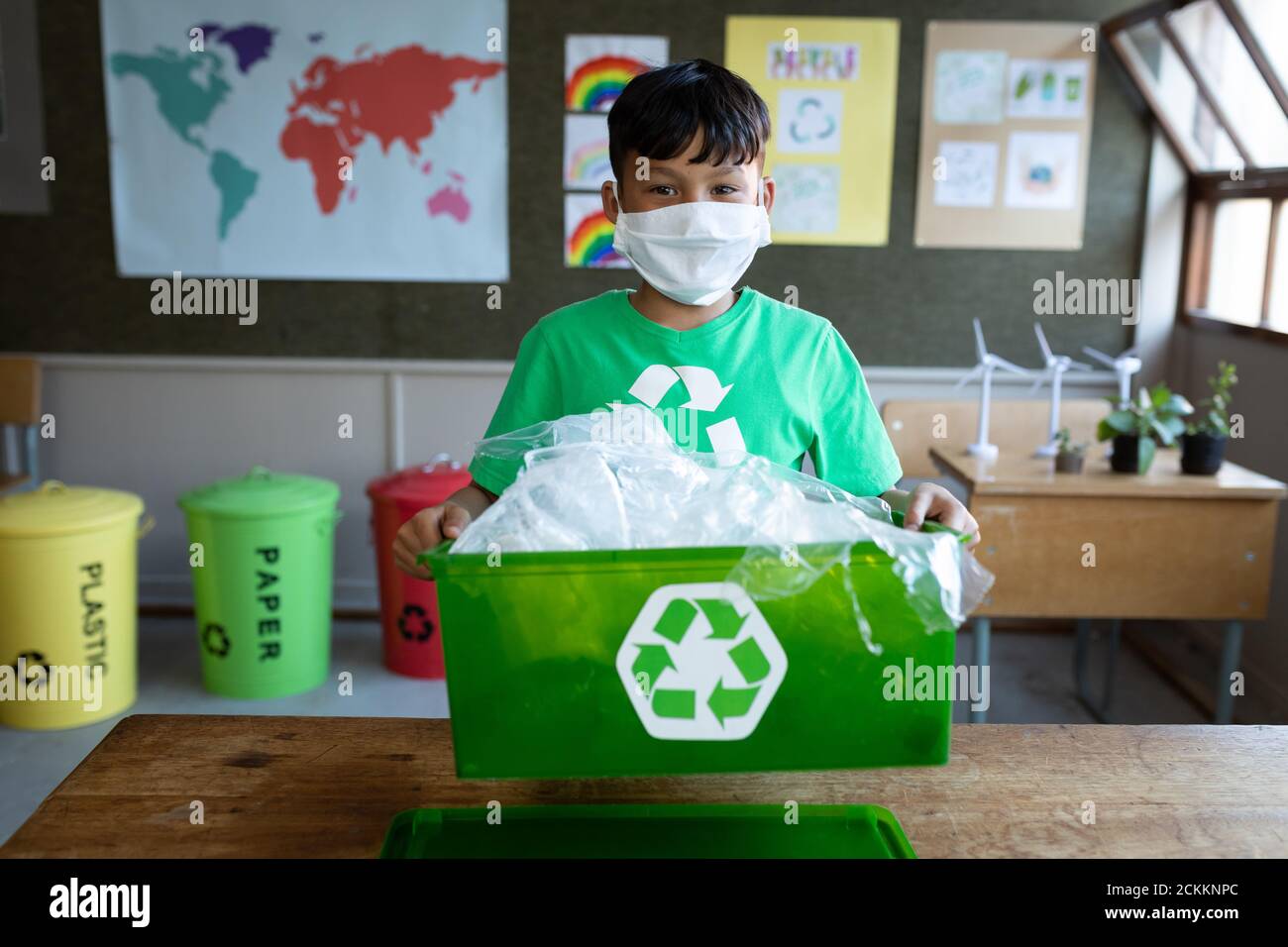 Portrait d'un garçon portant un masque facial tenant un récipient de recyclage en classe à l'école Banque D'Images