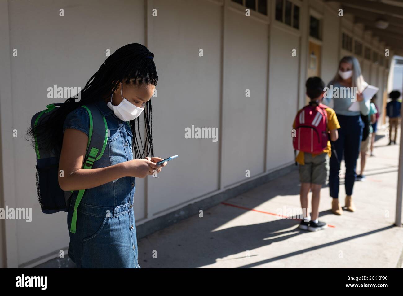 Fille portant un masque facial utilisant un smartphone à l'école Banque D'Images