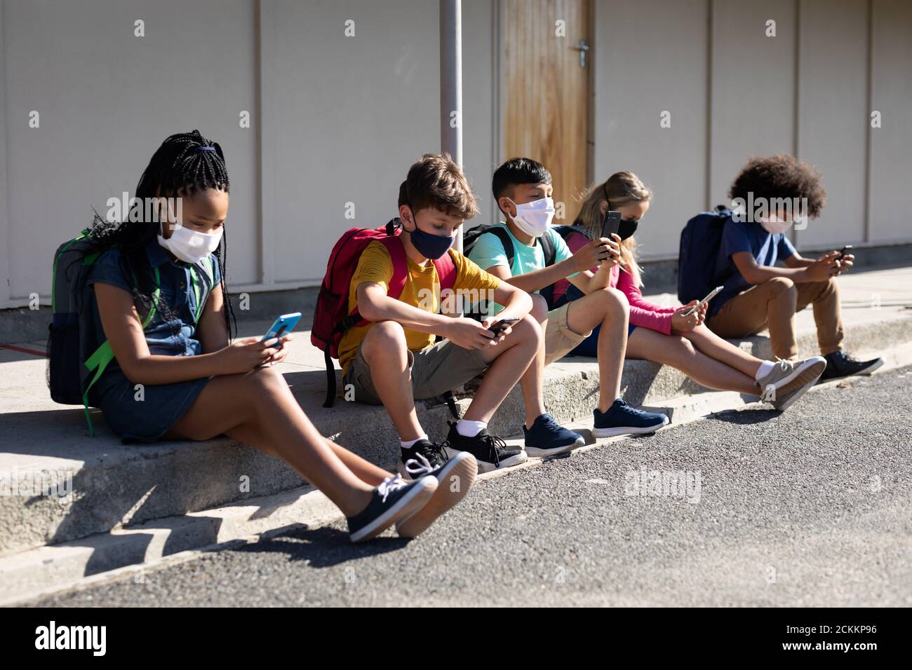 Groupe d'enfants portant un masque facial avec un smartphone lorsqu'ils sont assis ensemble Banque D'Images