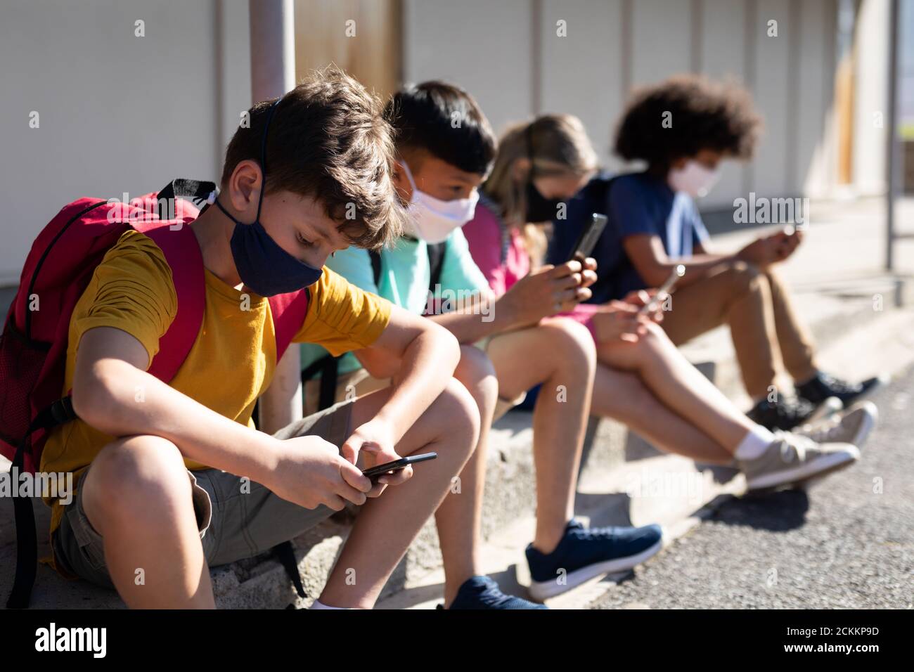 Groupe d'enfants portant un masque facial avec un smartphone lorsqu'ils sont assis ensemble Banque D'Images