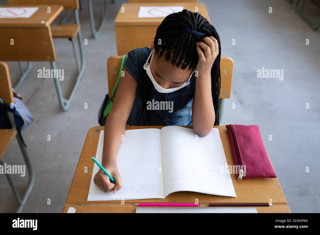 Vue de dessus d'une fille portant un masque de visage écrivant pendant qu'elle est assise sur son bureau à l'école Banque D'Images