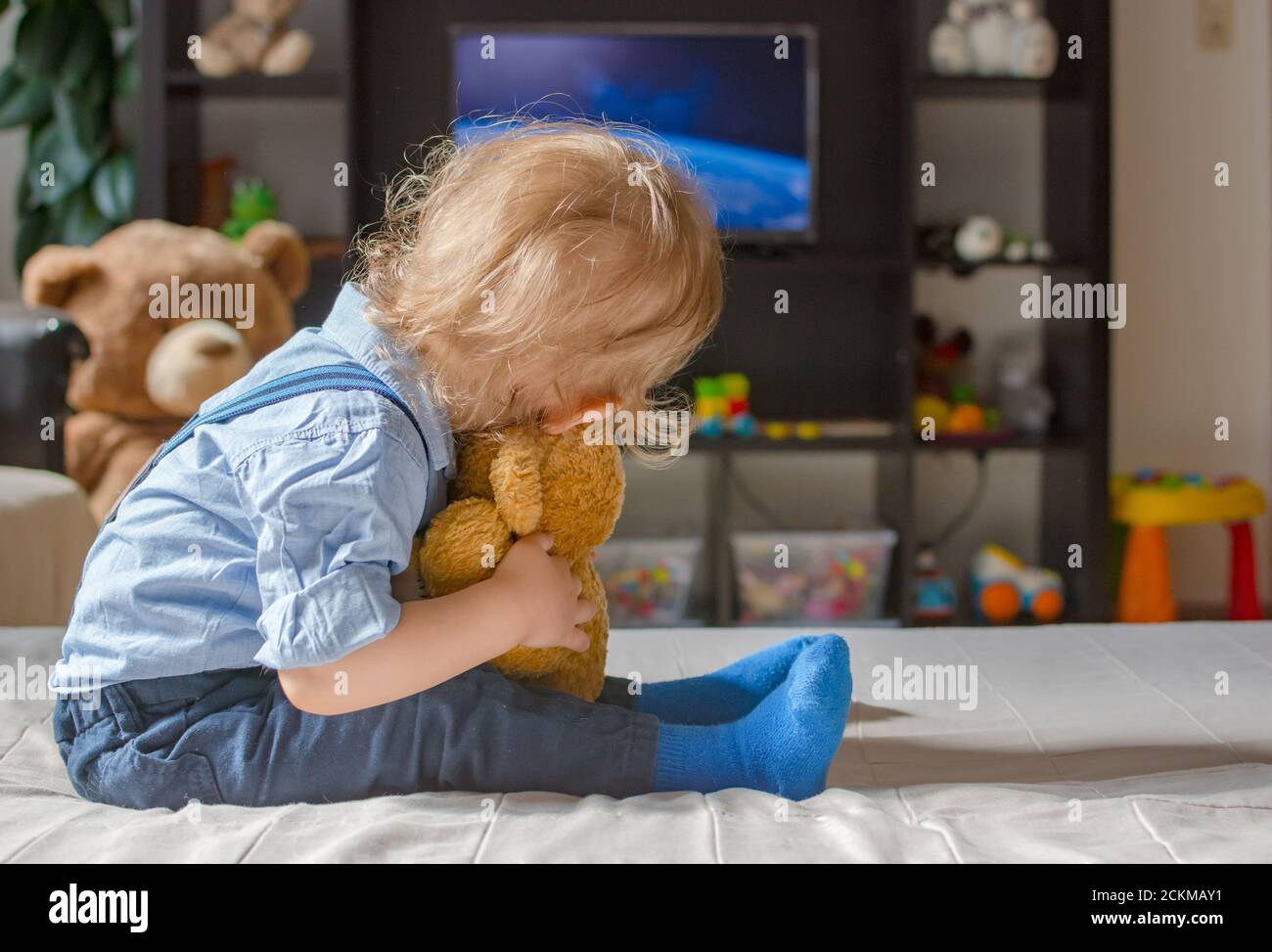 Un joli petit garçon et son ours en peluche regardant la télé s'asseoir sur un canapé dans le salon à la maison Banque D'Images