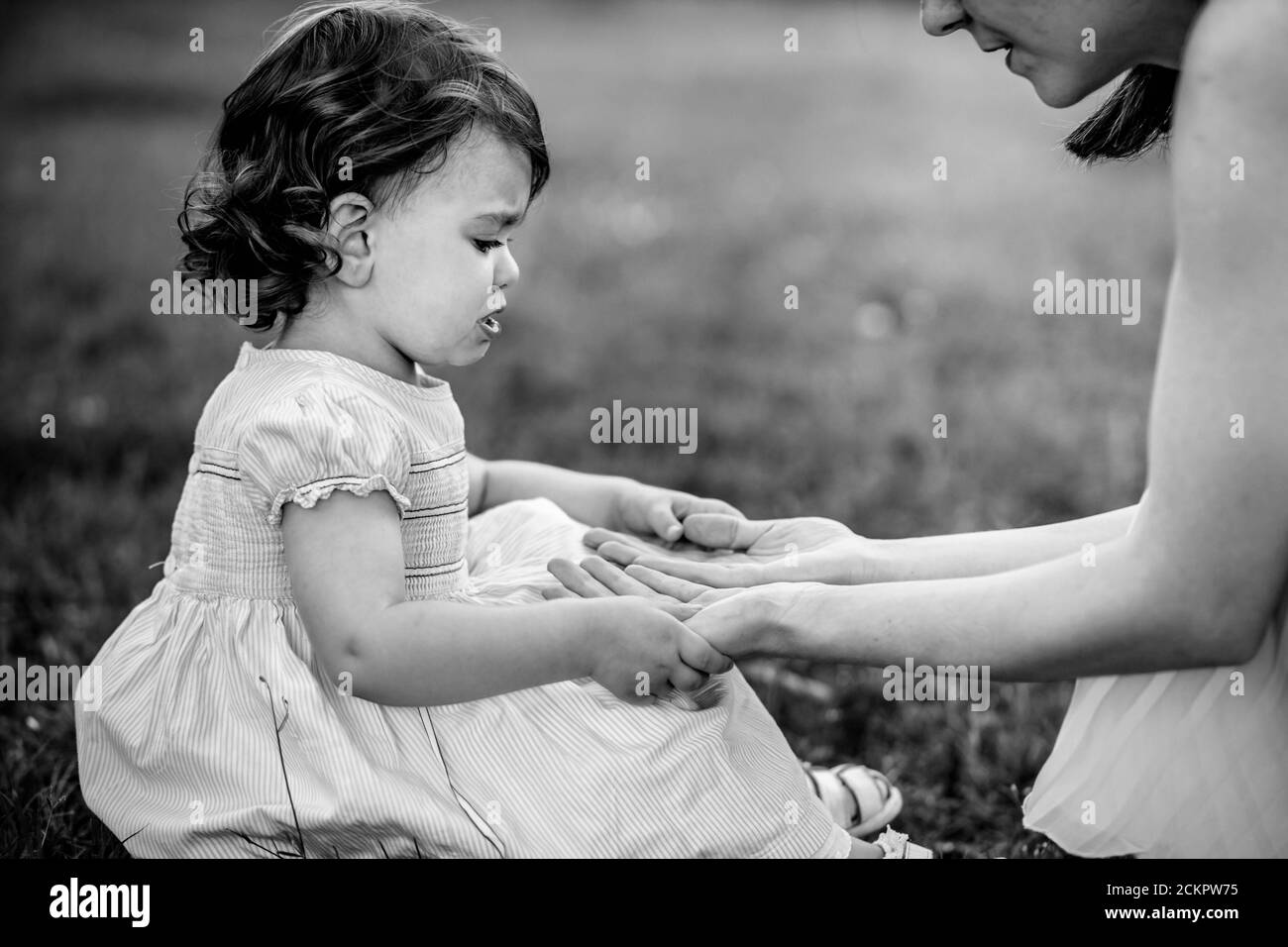 Photo portrait noir et blanc d'une petite fille maurie qui a l'air bouleversée, tenant les mains de maman pour le confort Banque D'Images