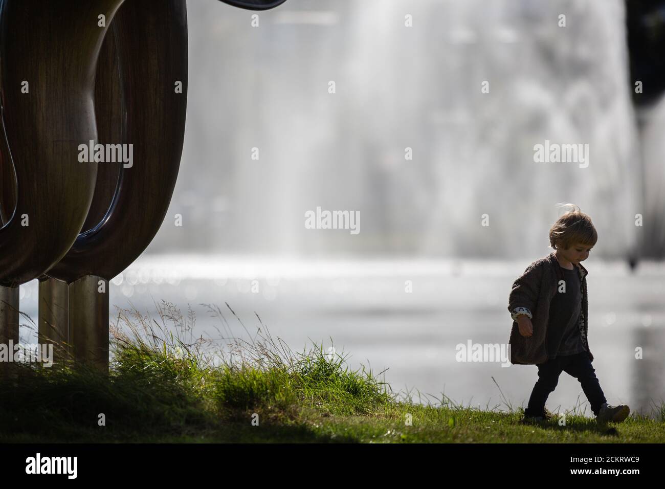 Petit garçon à côté d'une grande sculpture, fontaine derrière Banque D'Images