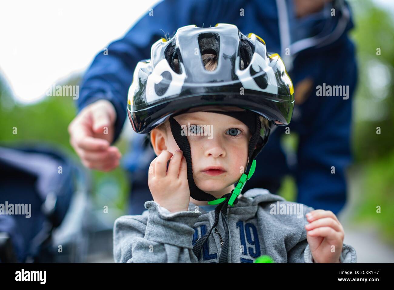 jeune garçon avec un grand casque de vélo, les papas se penchent la main pour ajuster la sangle Banque D'Images