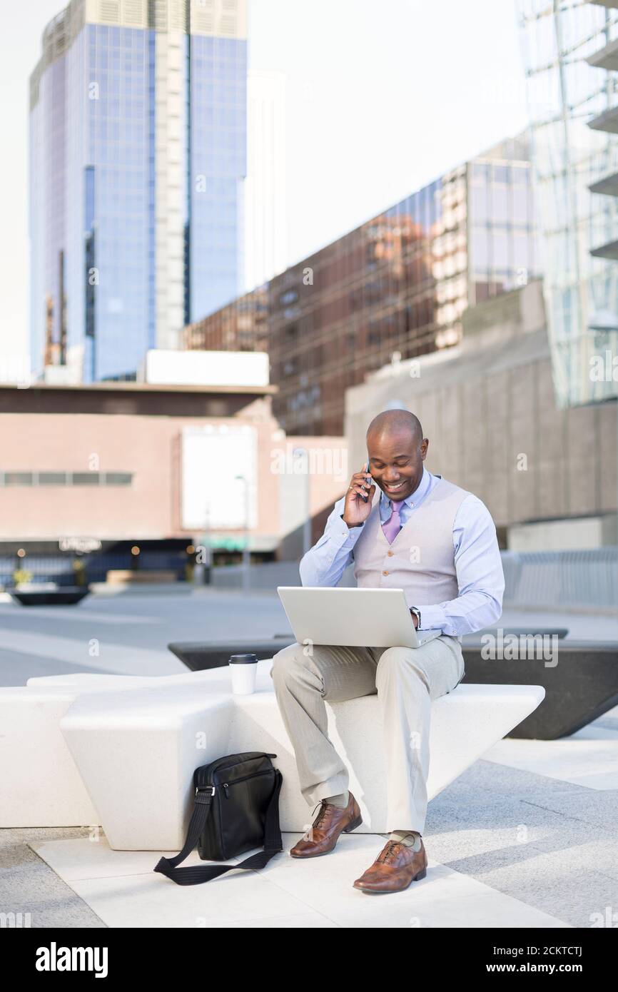 Homme d'affaires noir parlant à son smartphone tout en conduisant son ordinateur portable dans la rue. Concept de nouvelles façons d'affaires. Espace pour le texte. Banque D'Images