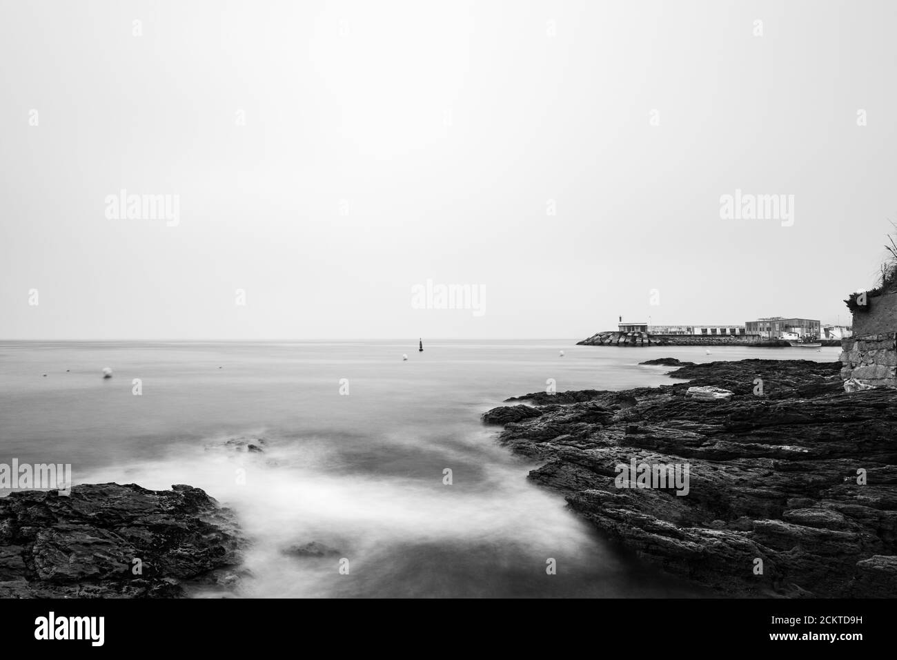 Rochers et petit phare lors d'une soirée calme et brumeuse dans le Rias Baixas en Galice, Espagne. Exposition longue, monochrome. Banque D'Images