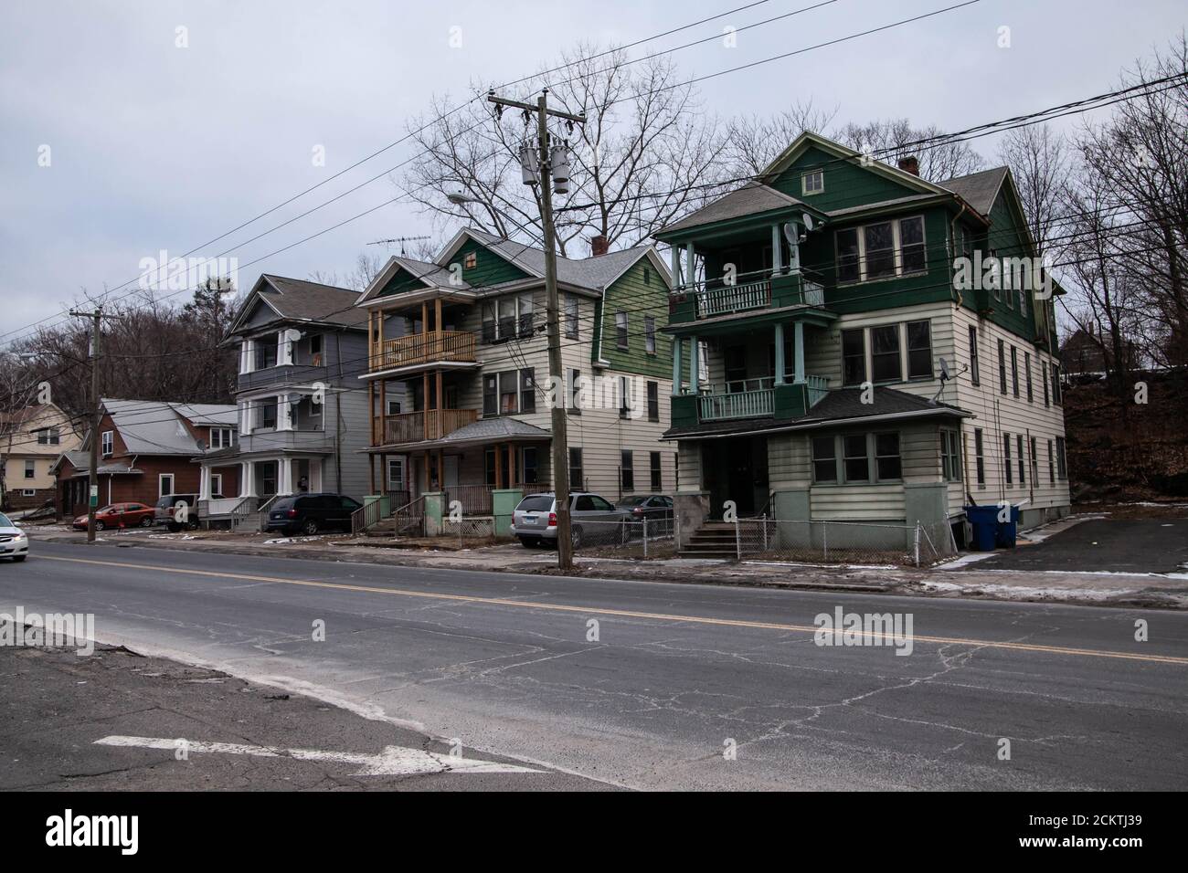 Le quartier délabré avec des bâtiments décrépits entouré de clôtures à chaînage et de vieilles voitures garées à côté lors d'une sombre journée d'hiver gris. Banque D'Images