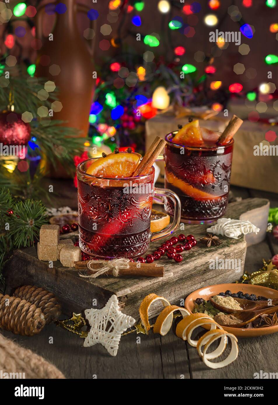 Vin chaud avec tranche d'orange, bâton de cannelle sur fond de guirlande lumineuse festive. Style sombre Banque D'Images