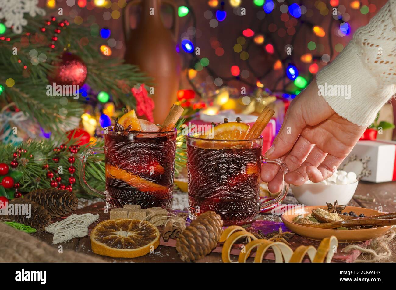 Une femme prend une tasse de vin chaud avec une tranche d'orange sur fond de guirlande lumineuse festive. Banque D'Images