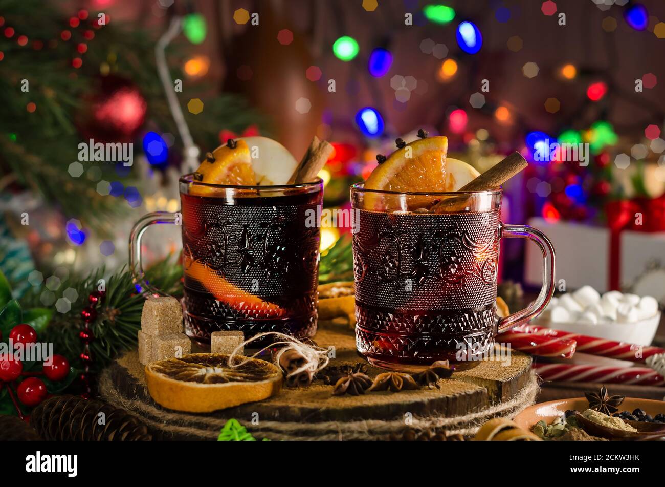Vin chaud avec tranche d'orange, bâton de cannelle sur fond de guirlande lumineuse festive. Style sombre Banque D'Images