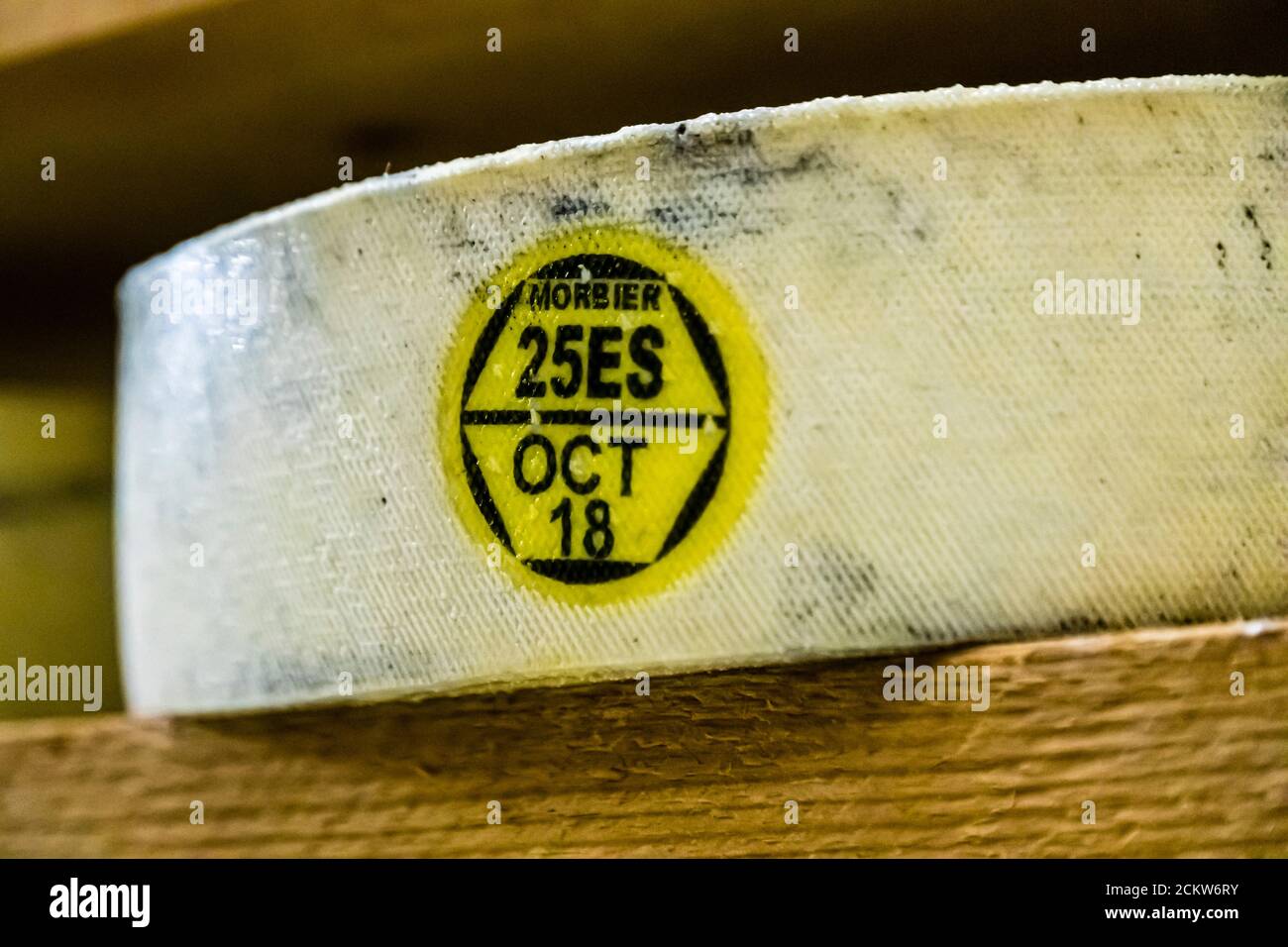 Une étiquette de contrôle jaune et noire portant la mention "MORBIER 25ES OCT 18" est attachée à la croûte d'une meule de fromage à la Fruitière des Lacs près de Pontarlier dans la région Bourgogne-Franche-Comté en France. L'étiquette identifie la meule comme du Morbier, un autre fromage traditionnel à cru de Franche-Comté connu pour sa couche distinctive de cendre au centre, et enregistre la date de production d'octobre 2018. Banque D'Images