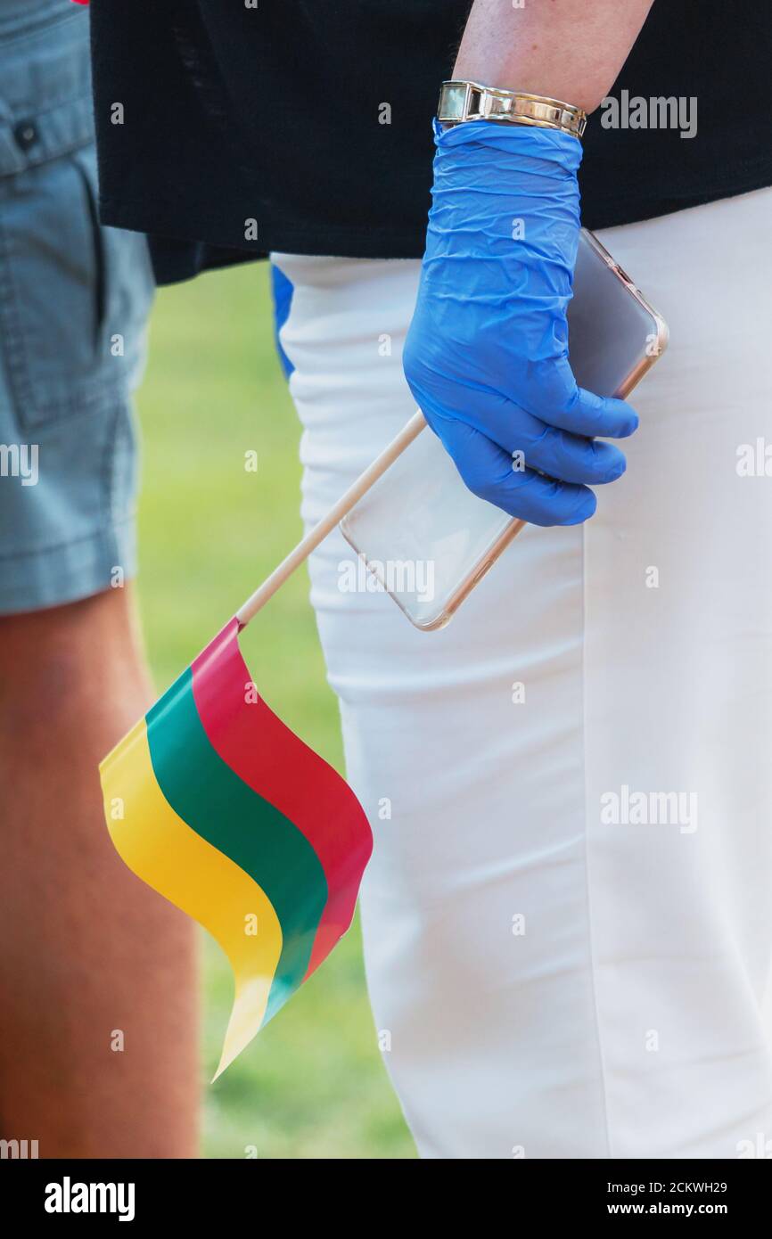 La main avec un gant tient un smartphone et un drapeau lituanien. Banque D'Images