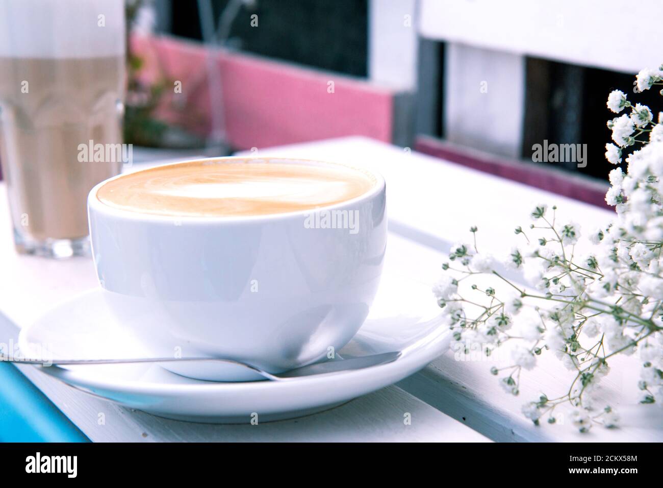 Cappuccino dans une tasse en céramique blanche et bouquet de petites fleurs blanches sur un banc en bois. Café rustique en plein air le matin. Routine du matin. Gypsophila fl Banque D'Images