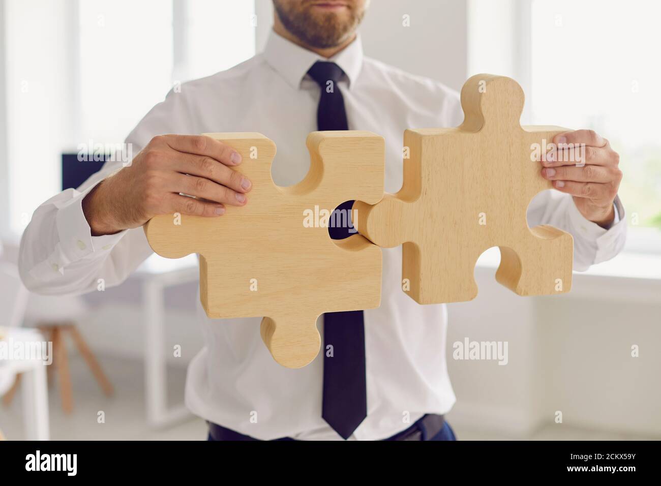 Un homme d'affaires ou un directeur d'entreprise en tenue de bureau se joint à deux pièces de puzzle Banque D'Images
