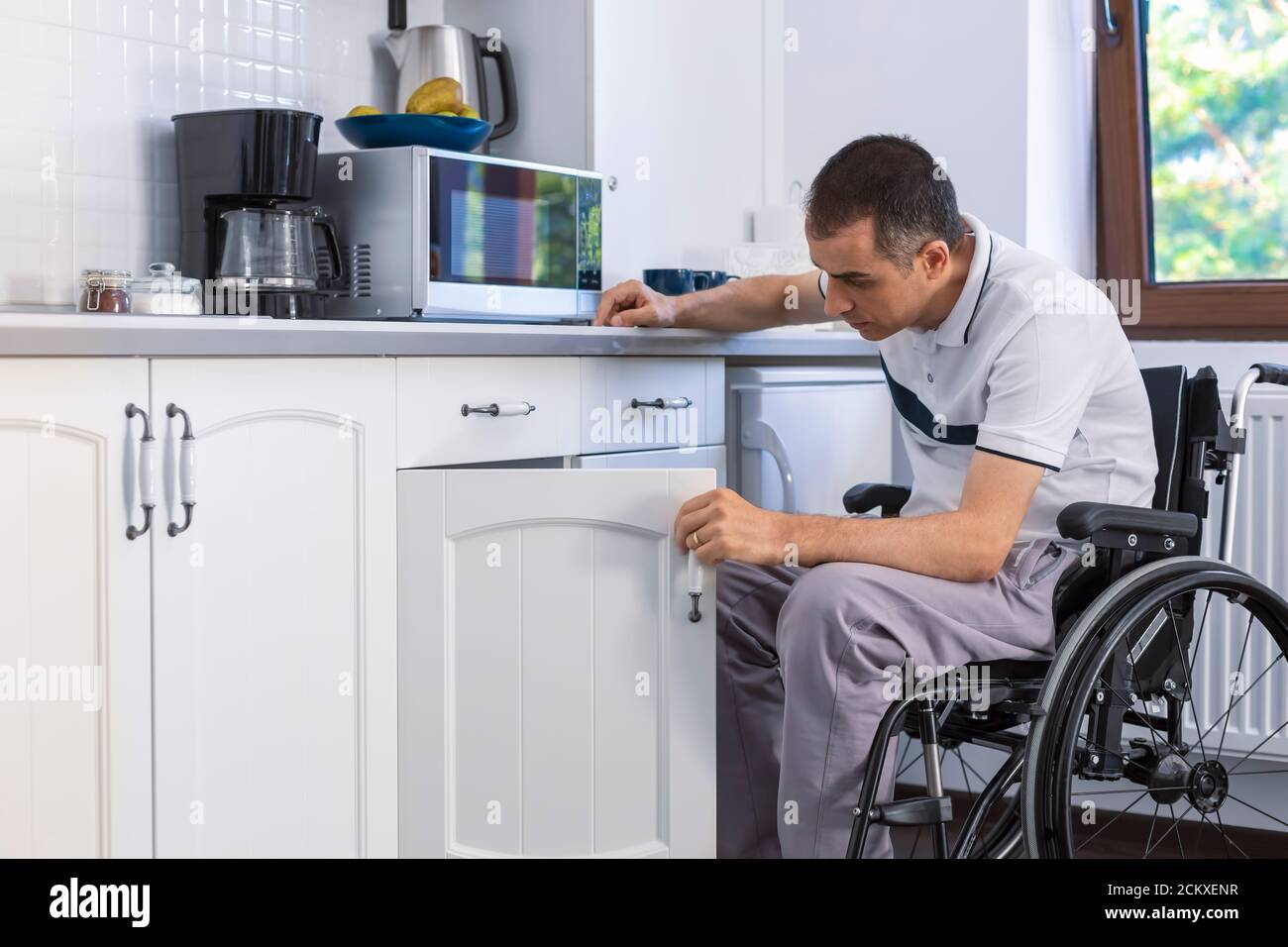 Jeune homme handicapé assis en fauteuil roulant dans la cuisine. Concentrez-vous sur son visage. Banque D'Images