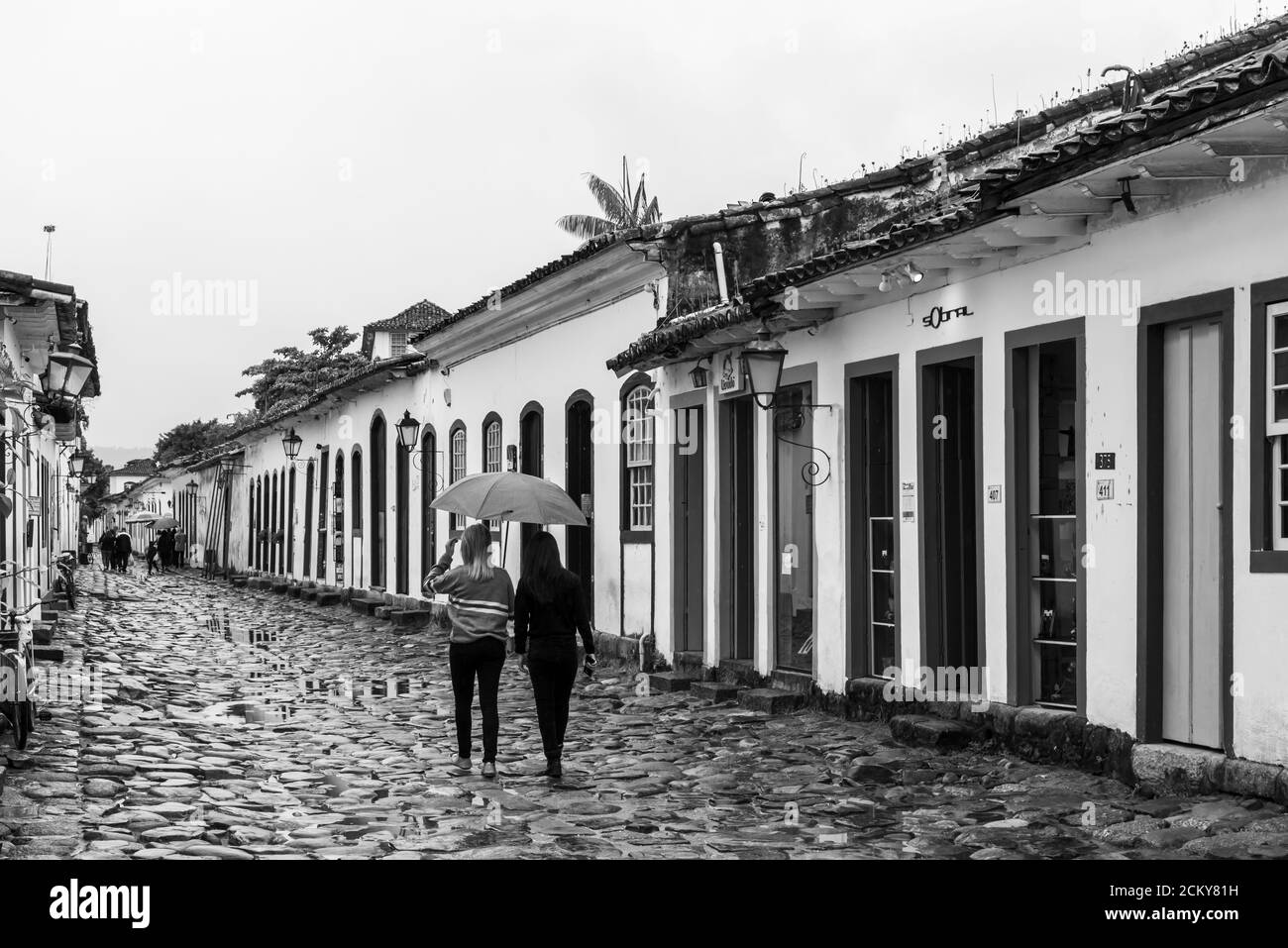 Photo noir et blanc de deux filles marchant sous un parapluie pendant un jour pluvieux dans la rue d'un ville historique au brésil Banque D'Images