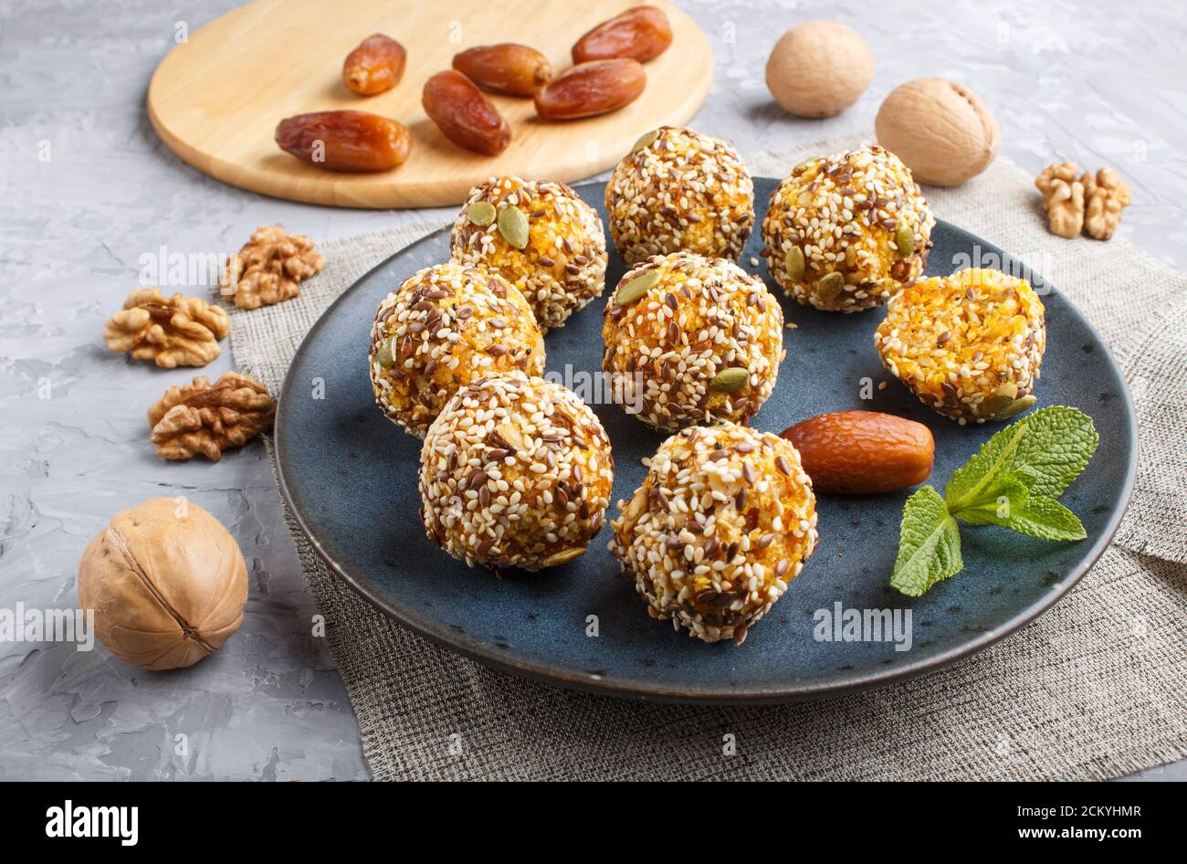 Galettes de boules d'énergie avec abricots séchés, sésame, lin, noix et dattes avec feuilles de menthe verte sur une plaque en céramique bleue sur fond de béton gris. Banque D'Images