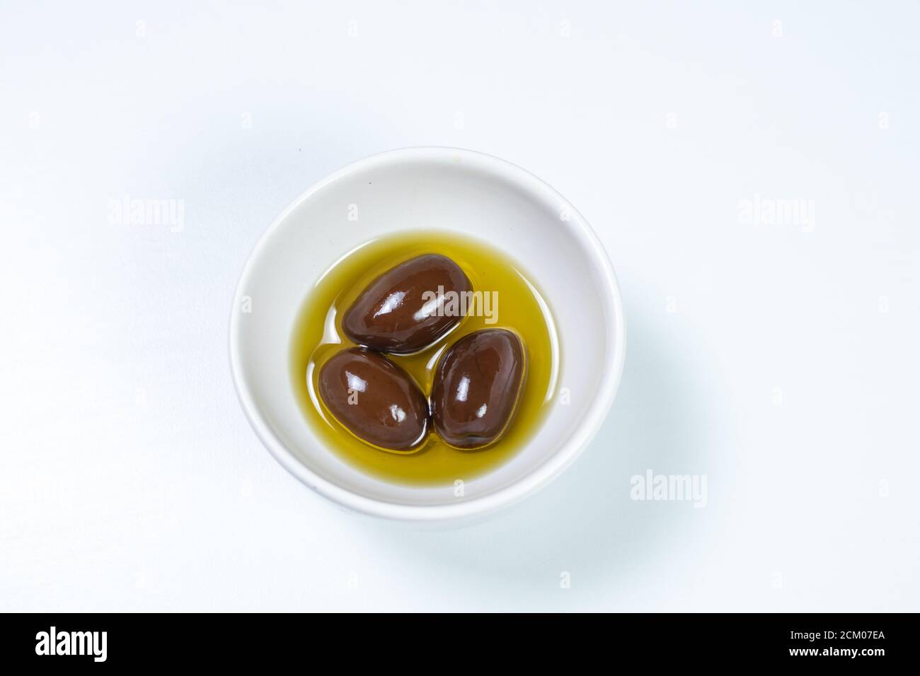 Olives noires dans une petite casserole avec de l'huile d'olive Une surface blanche arrière-plan vue de dessus Banque D'Images