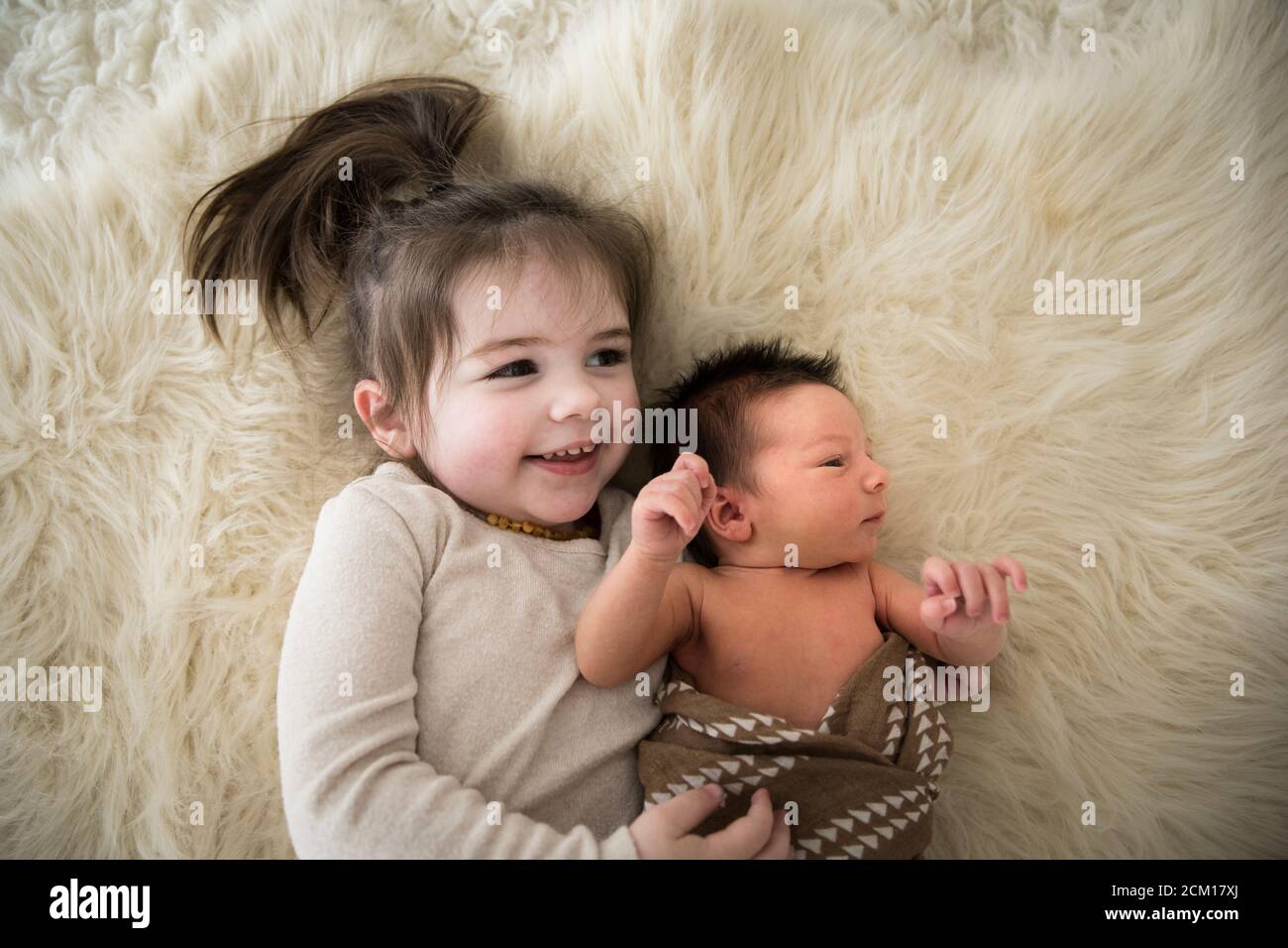 La grande sœur embrasse le nouveau-né frère tout en posant sur Fuzzy Rug Banque D'Images