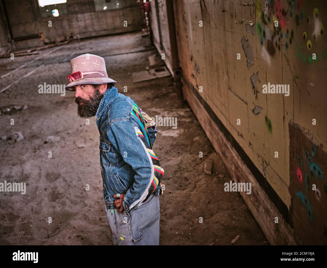 Un homme de mode éclectique regarde vers l'appareil photo dans un espace abandonné. Banque D'Images