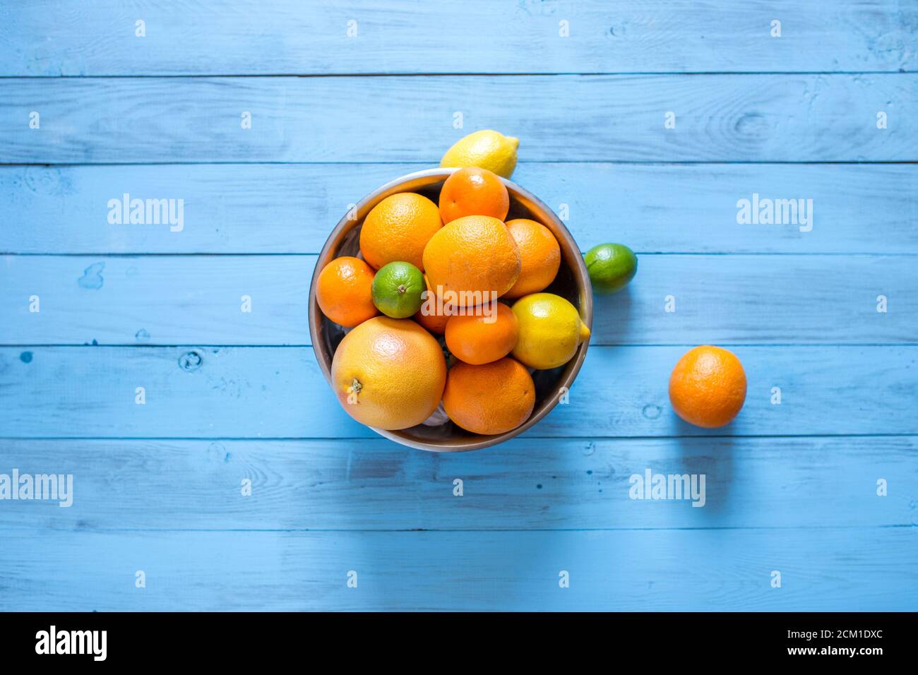Vue en grand angle des agrumes entiers mûrs et colorés comme les oranges, les mandarines, les limes, les pamplemousses et les citrons dans un bol sur fond de bois bleu avec Banque D'Images