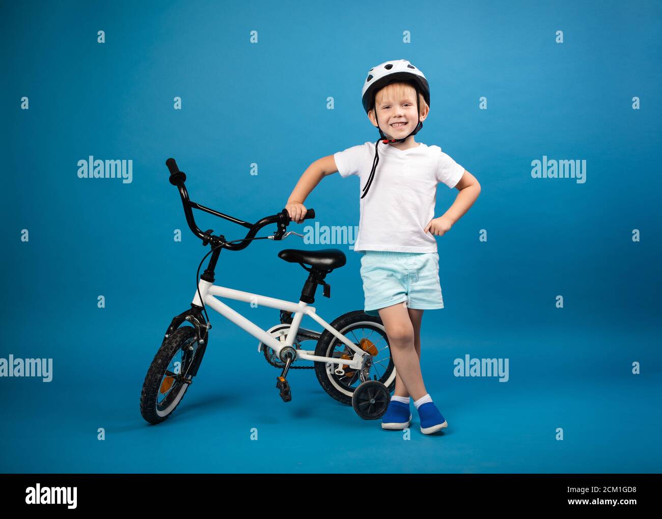 Un enfant tout-petit avec un vélo d'enfant et un casque de protection se tient sur un fond bleu et regarde dans la caméra. Studio photo pour des articles sur safe Banque D'Images