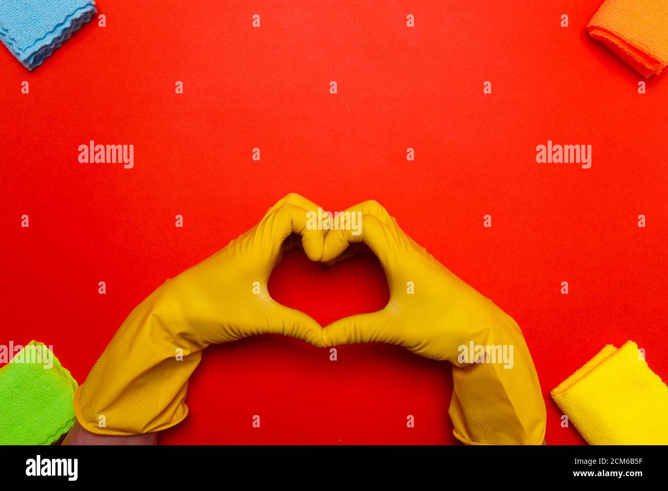 les mains dans des gants en caoutchouc orange au centre représentent un coeur sur un fond rouge. Banque D'Images