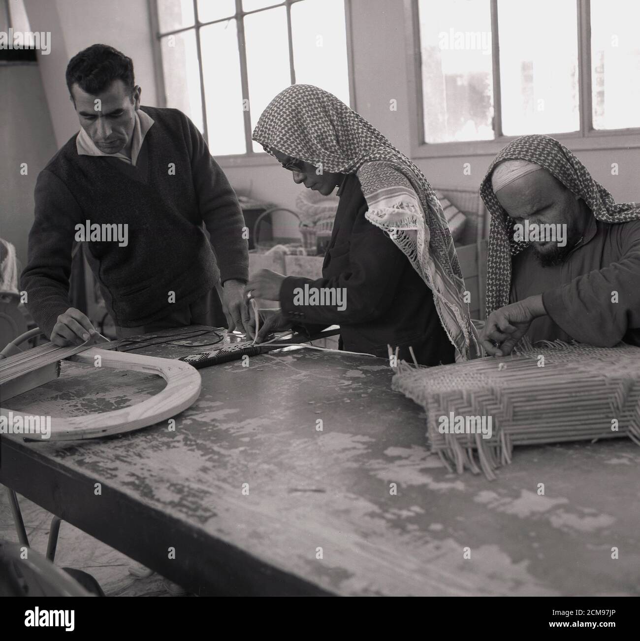 Dans les années 1960, deux hommes arabes à vue partielle dans un atelier, filant le dos des chaises à l'intérieur d'un atelier, leur tuteur ou superviseur supervisant leur travail, Djeddah, Arabie Saoudite. Banque D'Images