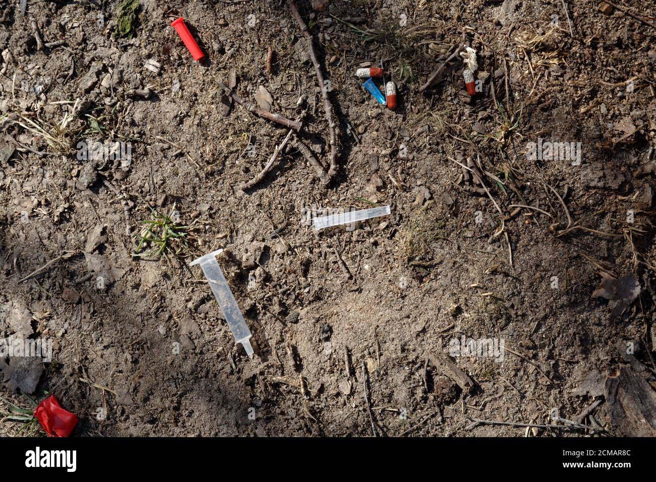 Une aiguille, une seringue, un capuchon et des comprimés médicaux cassés utilisés se trouvent sur le sol dans un parc de la ville Banque D'Images
