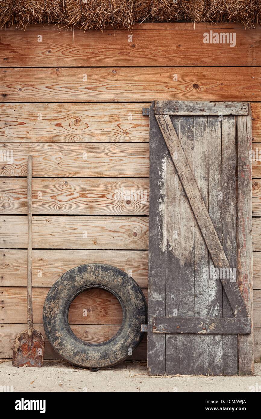 Ancienne porte de la grange, vieux pneu sale et pelle penchée contre la porte de la grange en bois d'une ferme Banque D'Images