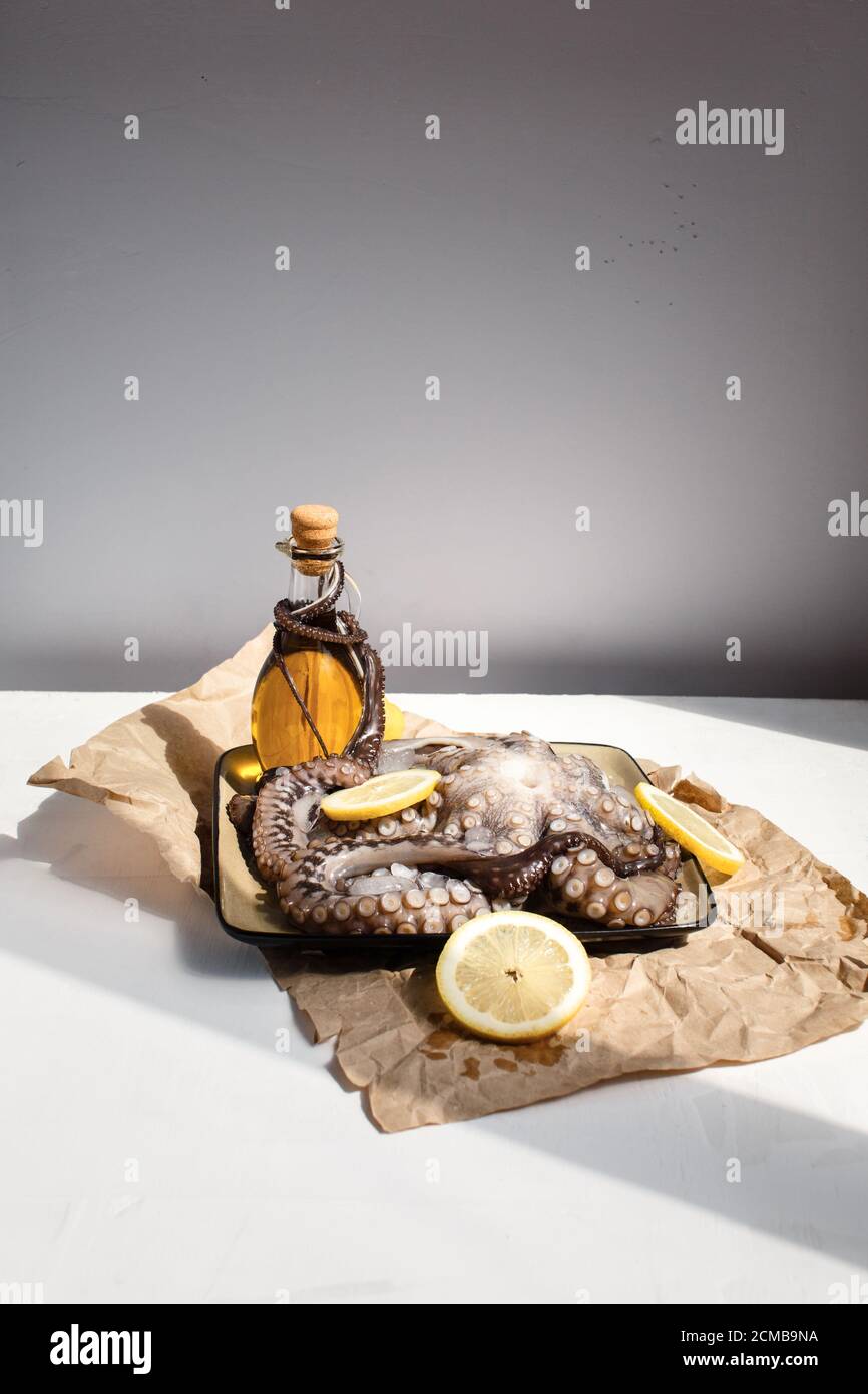 Fruits de mer, gros pieuvre cru sur une assiette avec des citrons et de l'huile d'olive prêts à être préparés, vue latérale Banque D'Images