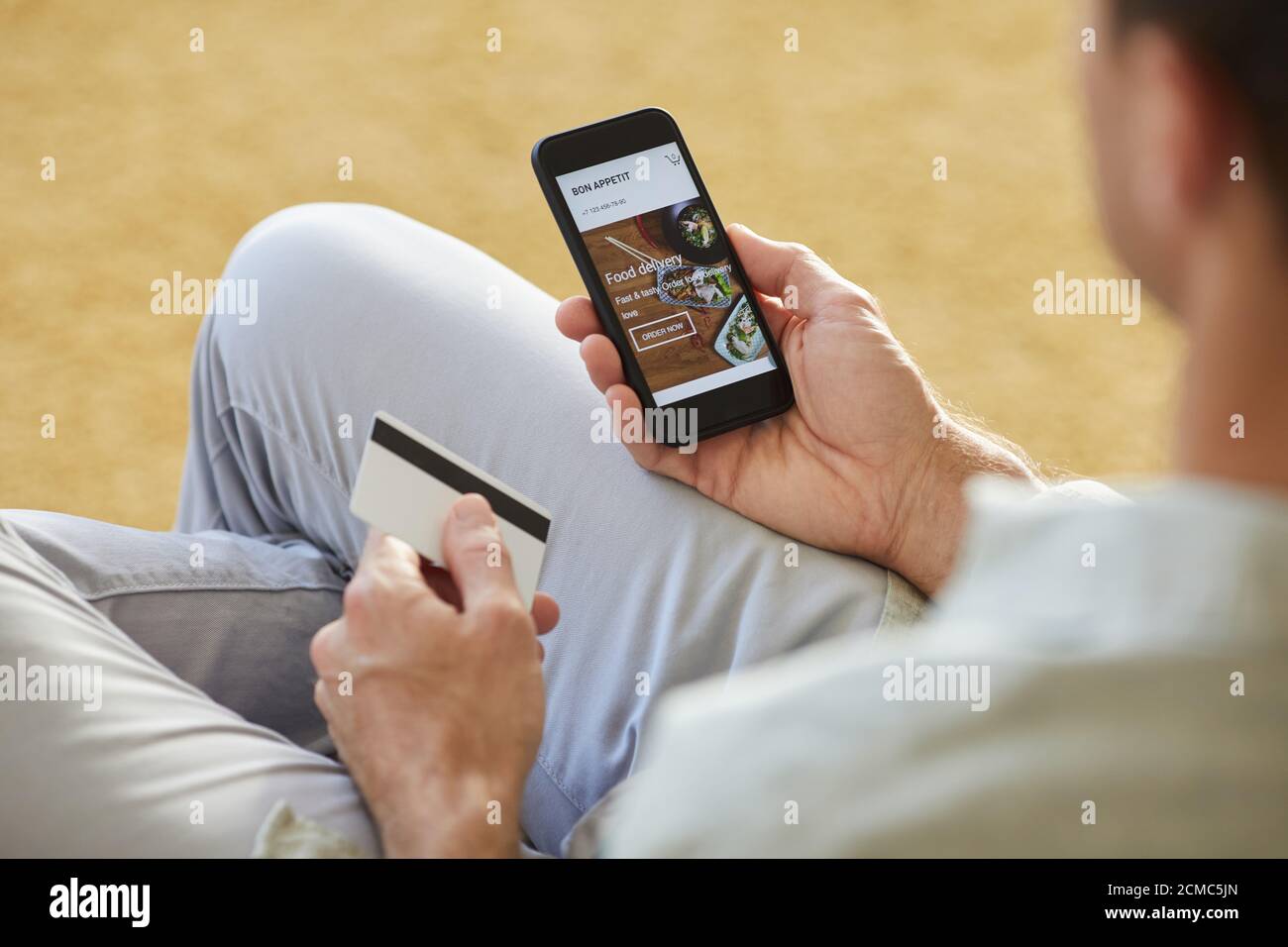 Gros plan d'un jeune homme utilisant un téléphone portable pour commander de la nourriture livraison il payant avec carte de crédit Banque D'Images