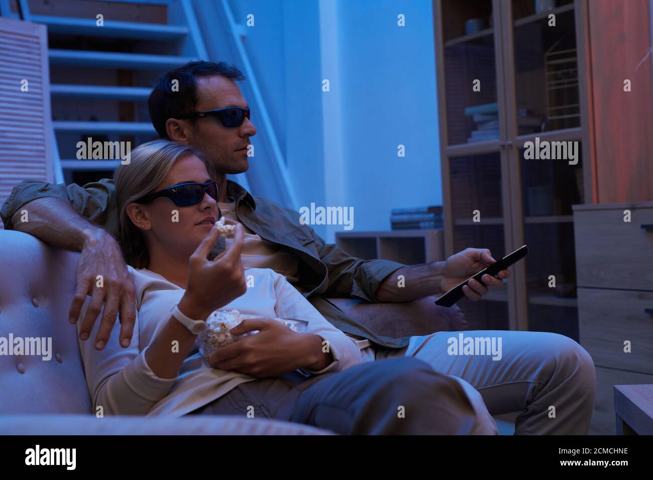 Jeune couple en lunettes 3D mangeant du pop-corn tout en étant assis canapé et regarder des films en 3D à la maison Banque D'Images