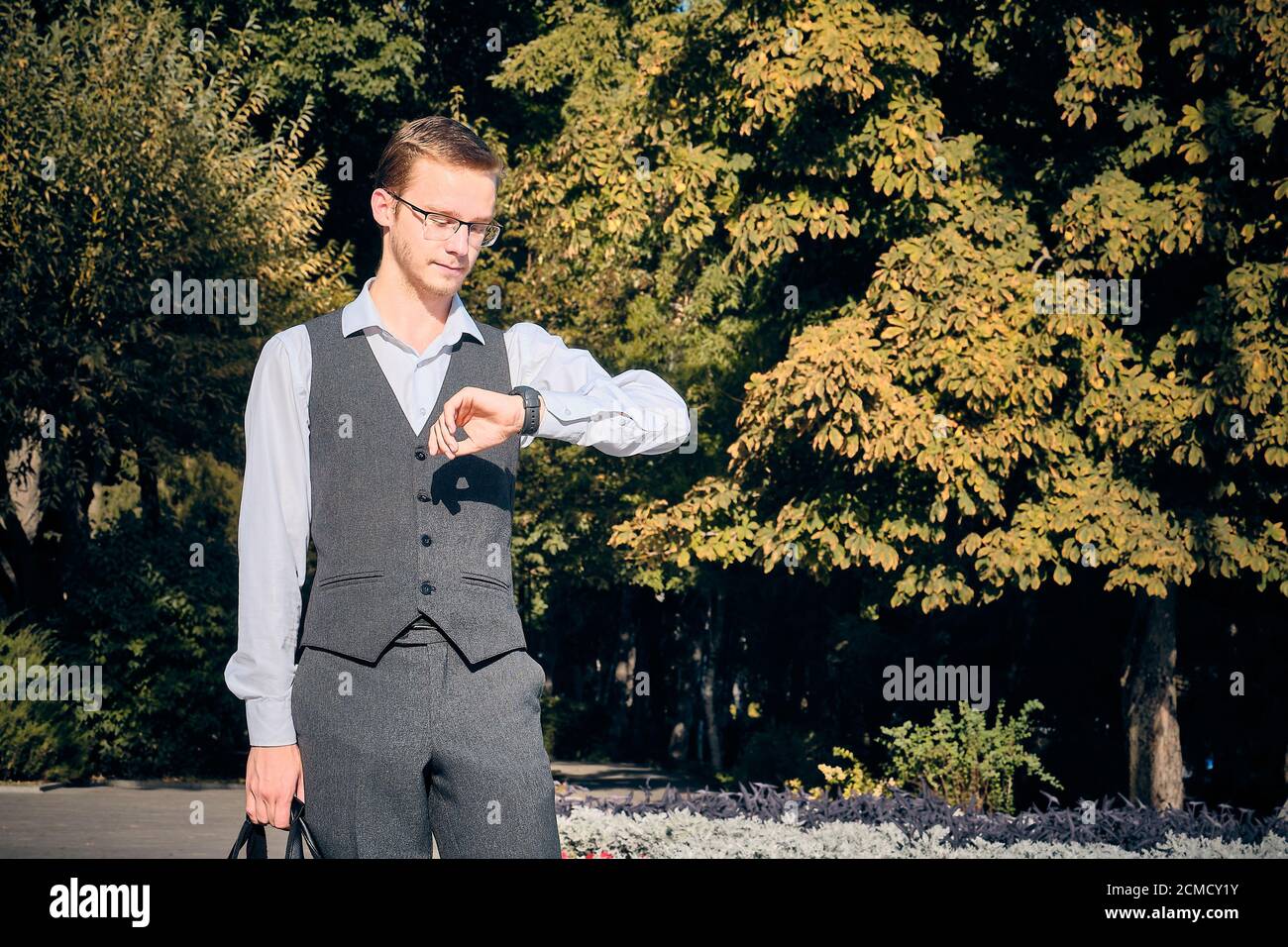Jeune homme habillé de blanc chemise et gilet de costume regarde dessus les montres au poignet Banque D'Images
