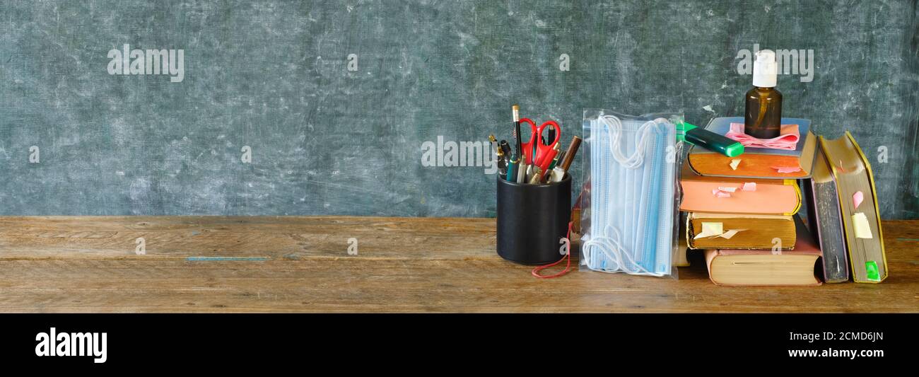 Fournitures scolaires et articles de prévention COVID 19 sur le bureau de la salle de classe avec des livres, des lunettes, des stylos sur fond de tableau noir. Retour à l'école pendant corona-viru Banque D'Images