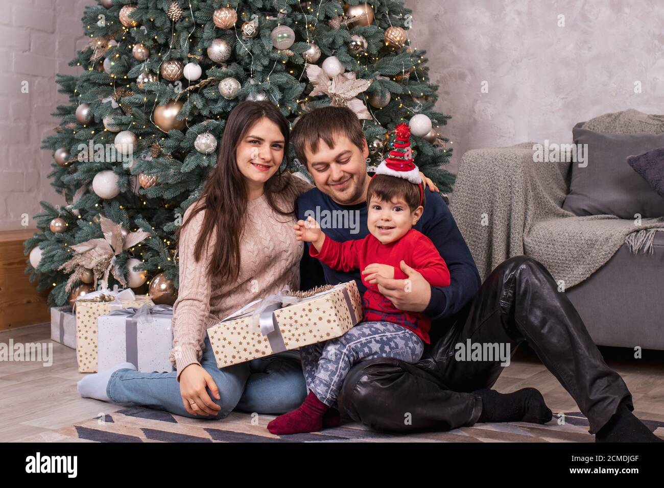 Maman, papa et jeune fils s'assoient près de l'arbre de Noël et tiennent des cadeaux. Vacances en famille nouvel an, cadeaux et un matin magique. Banque D'Images