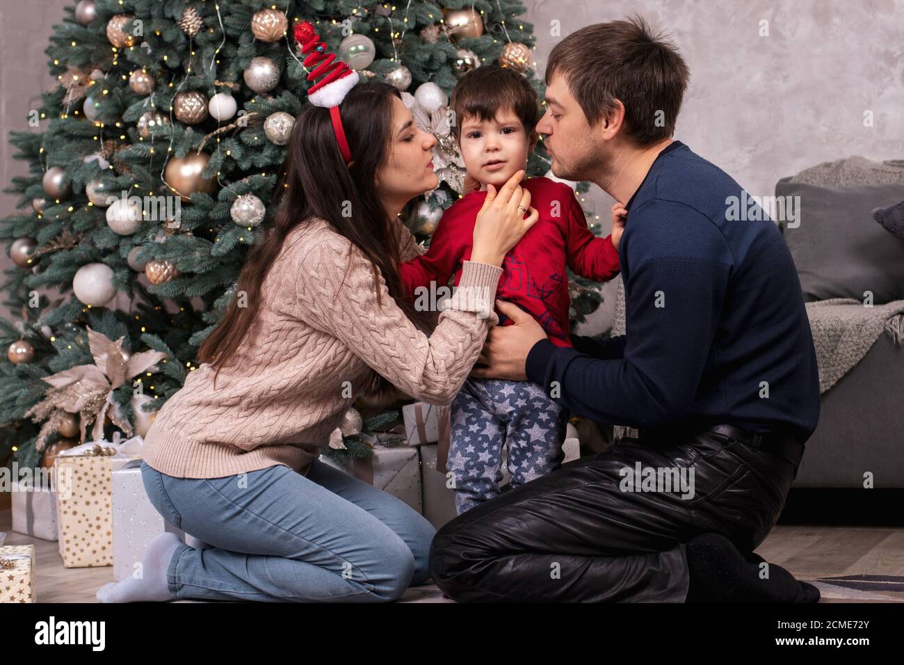 Maman et papa embrassent un jeune fils près de l'arbre de Noël. Bonne matinée du nouvel an en famille. Parents et enfant. Banque D'Images