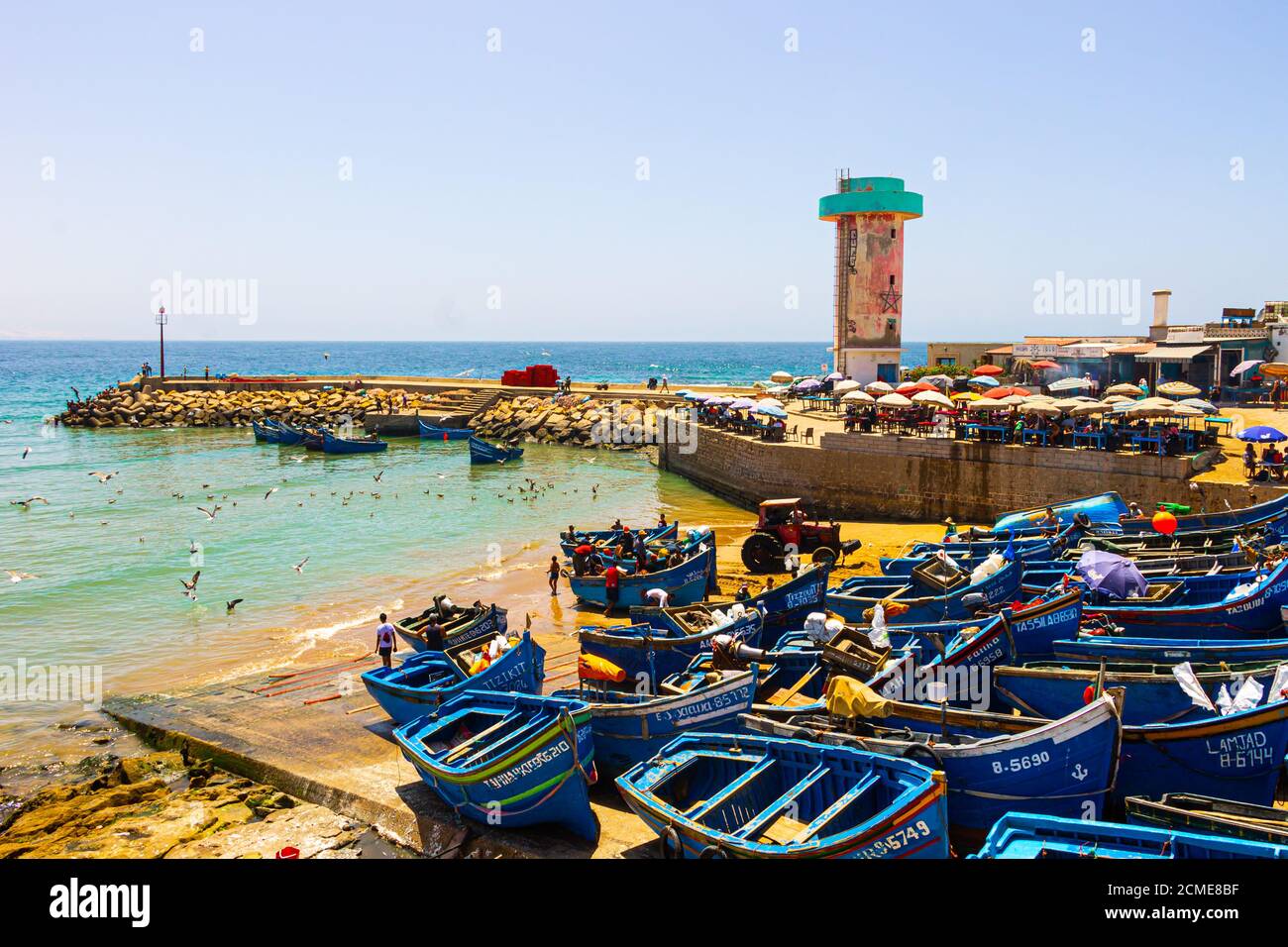 Agadir, Maroc - 14 AOÛT 2020 : le port d'Imesouane. Bateaux bleus, mouettes, tracteur, café, pêcheurs, personnes nageant et tour de contrôle Banque D'Images
