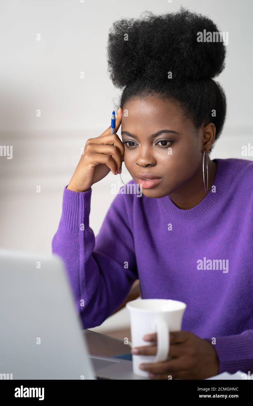 Femme étudiante millénaire afro-américaine concentrée avec conférence d'écoute de coiffure afro, regarder le webinaire sur ordinateur portable, étudier en ligne, se préparer à l'examen, ho Banque D'Images