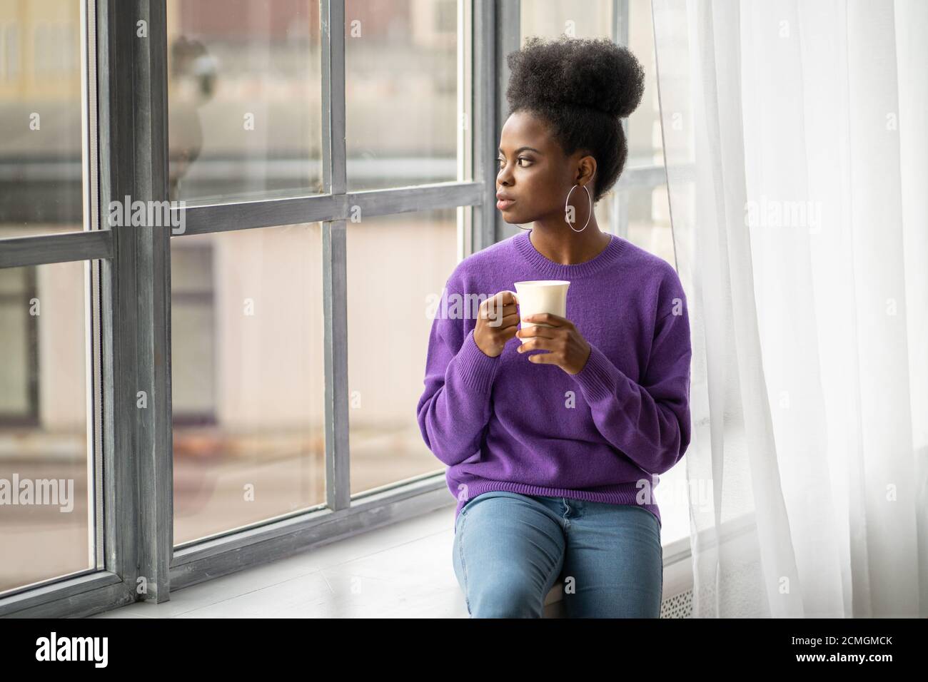 Femme biraciale millénaire afro-américaine pensive avec bijoux tendance boucles d'oreilles porter un chandail violet pensant, regardant à travers la fenêtre, tenant le coup Banque D'Images