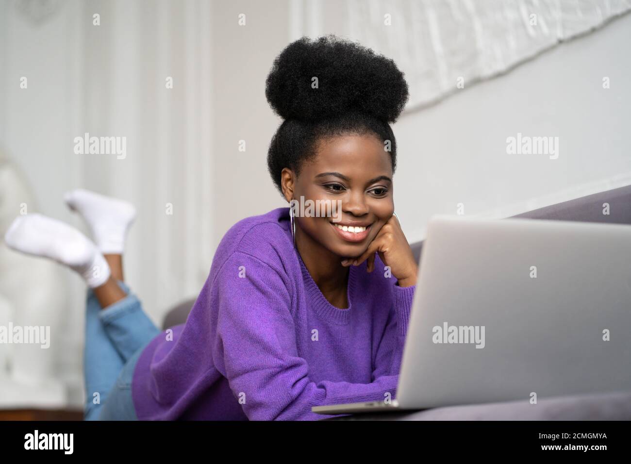 Souriante afro-américaine femme millénaire avec une coiffure afro porter un chandail violet allongé sur un canapé, se reposer, regarder la webcam de caméra et parler sur un vi Banque D'Images