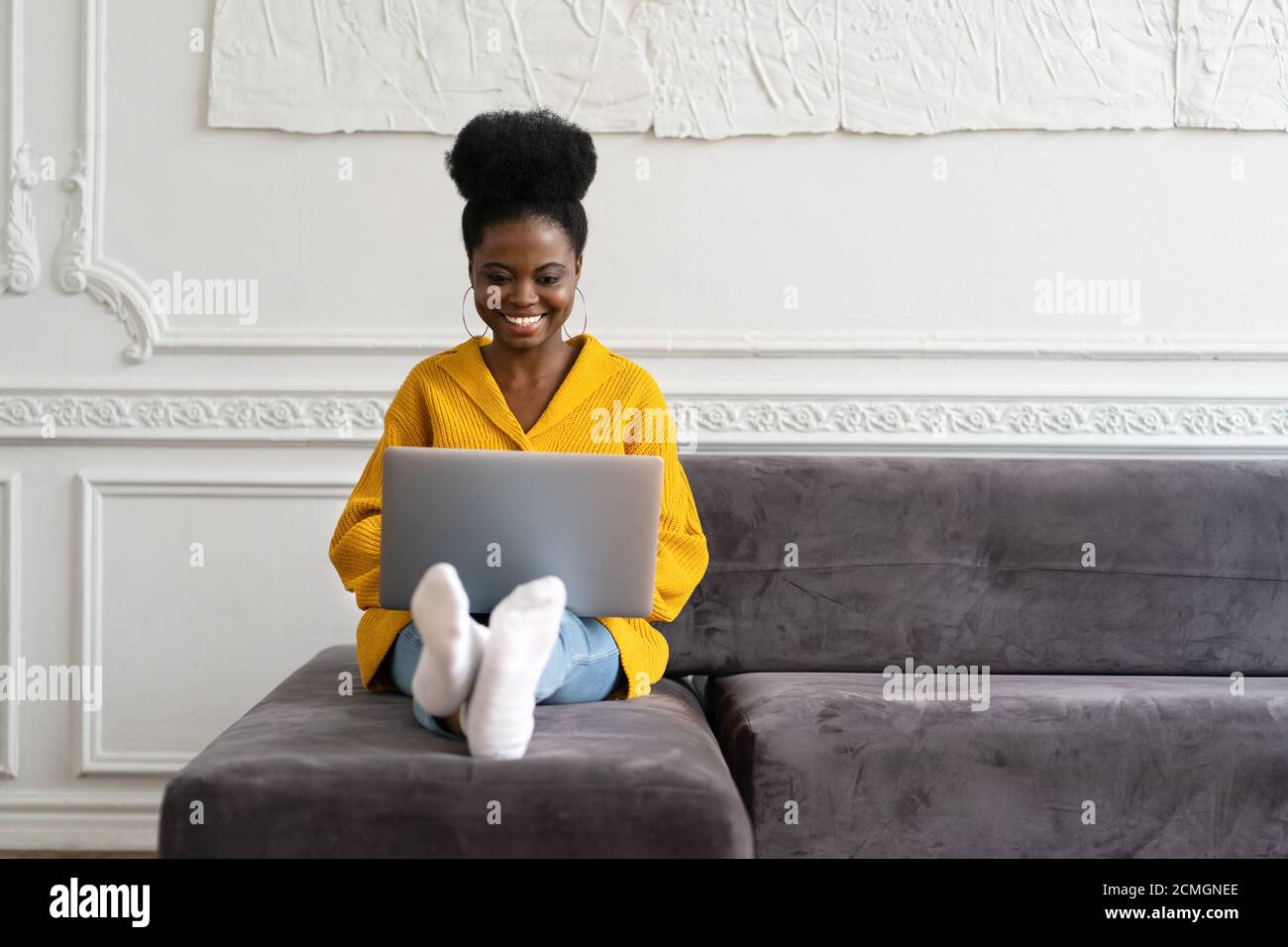Souriante afro-américaine femme millénaire avec une coiffure afro porter un gilet jaune assis sur un canapé, se reposer, regarder un appareil photo webcam et parler sur un Banque D'Images