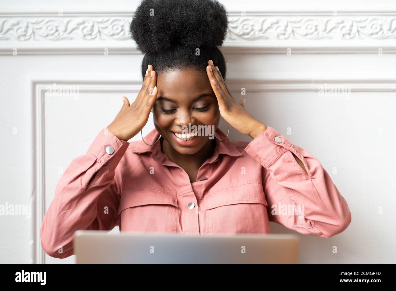 Joyeuse femme afro-américaine millénaire avec une coiffure afro porter une chemise rose regarder un film comique sur un ordinateur portable, bavarder avec des amis par appel vidéo Banque D'Images