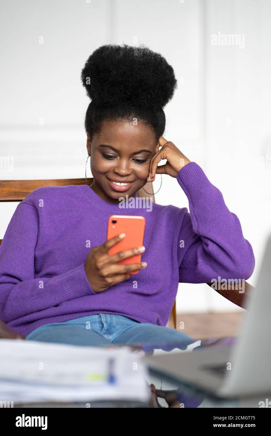 Gros plan portrait de la jeune femme millénaire afro-américaine en bijoux tendance grandes boucles d'oreilles porter un chandail violet assis, en utilisant un smartphone et en tapant M. Banque D'Images