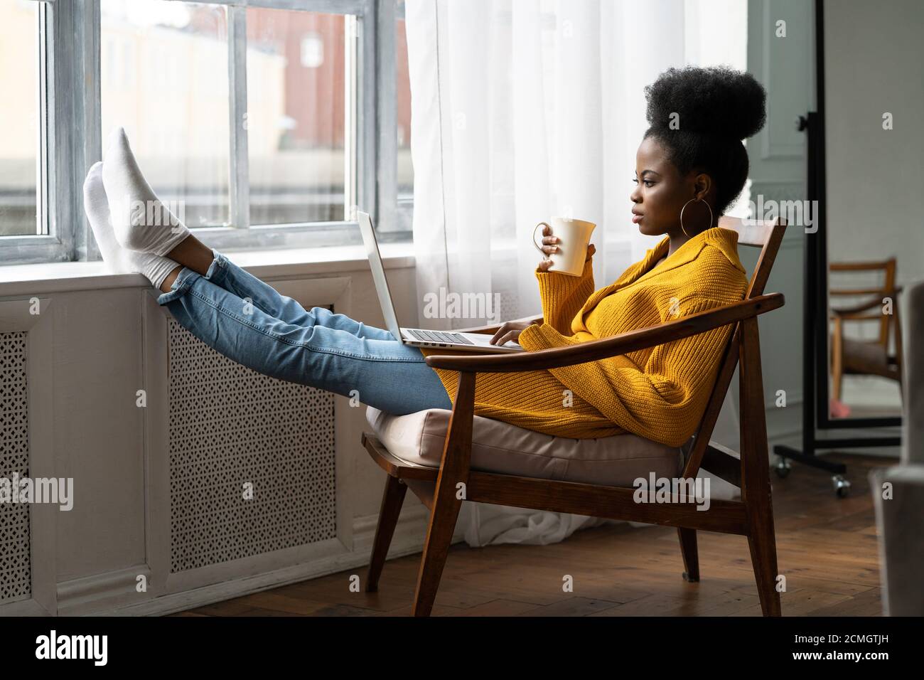 Femme afro-américaine freelance avec afro coiffure porter gilet jaune repos, assis sur une chaise, jambes penchées sur le seuil de la fenêtre, étudier à distance, wor Banque D'Images